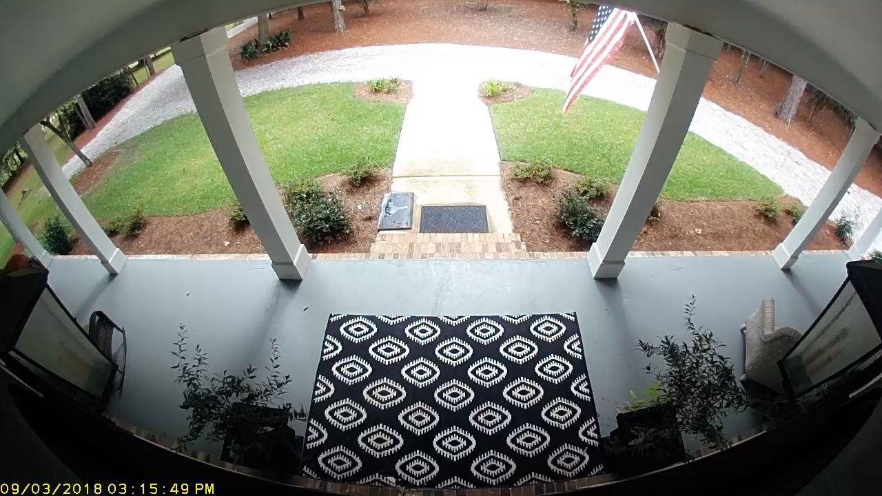 A home security camera photo above a front door looking out at the porch and front walkway.